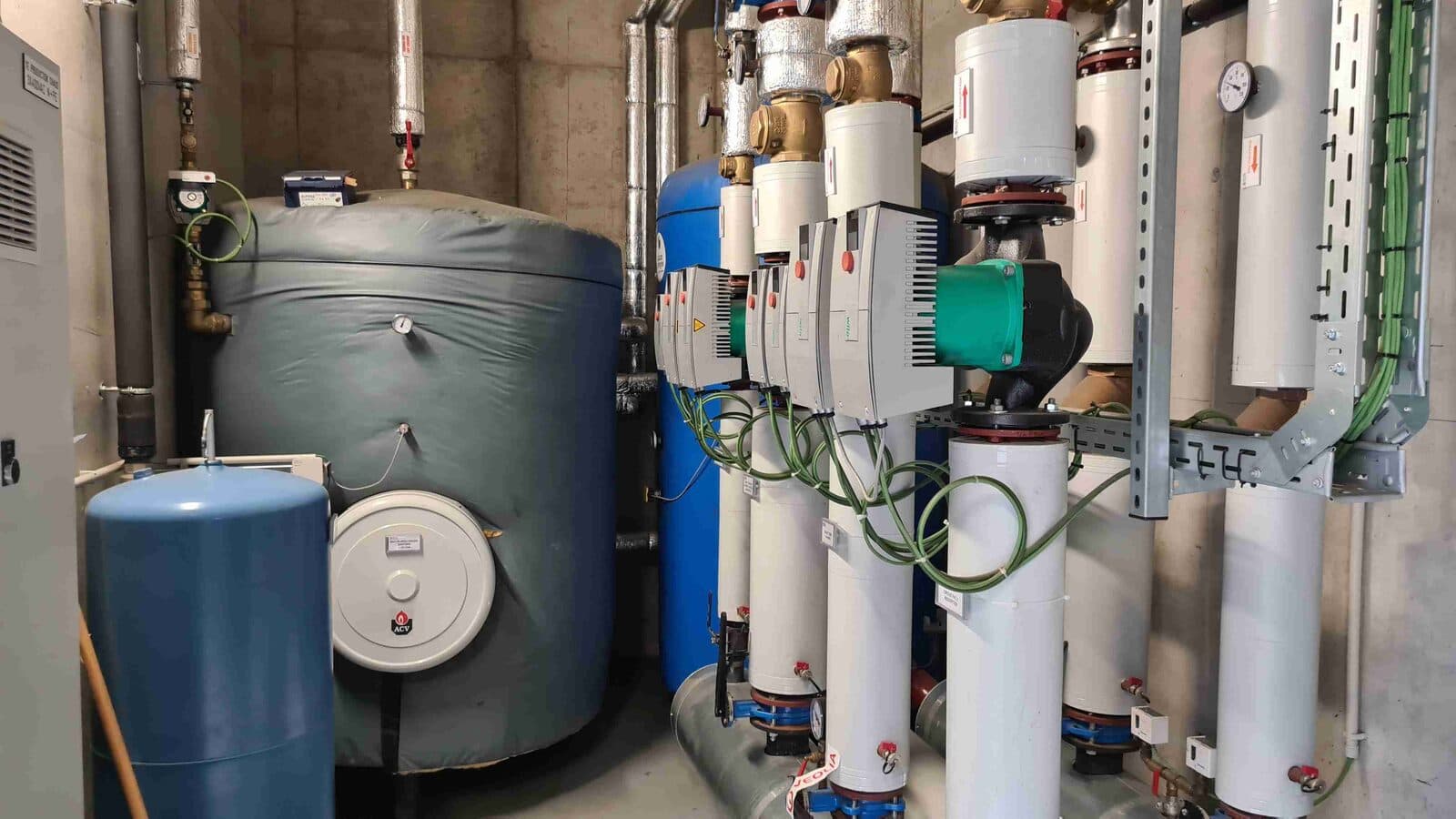 Ballons d'eau chaude sanitaire et circulateurs dans le local technique d'un bâtiment sportif